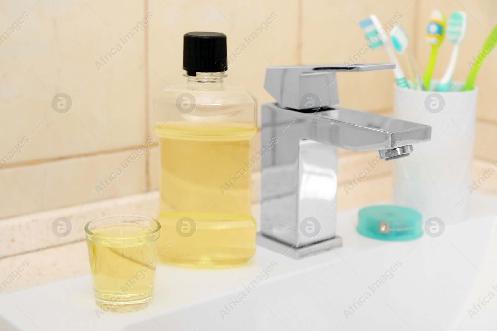 Photo of Mouthwash and holder with toothbrushes on sink in bathroom. Teeth and oral care