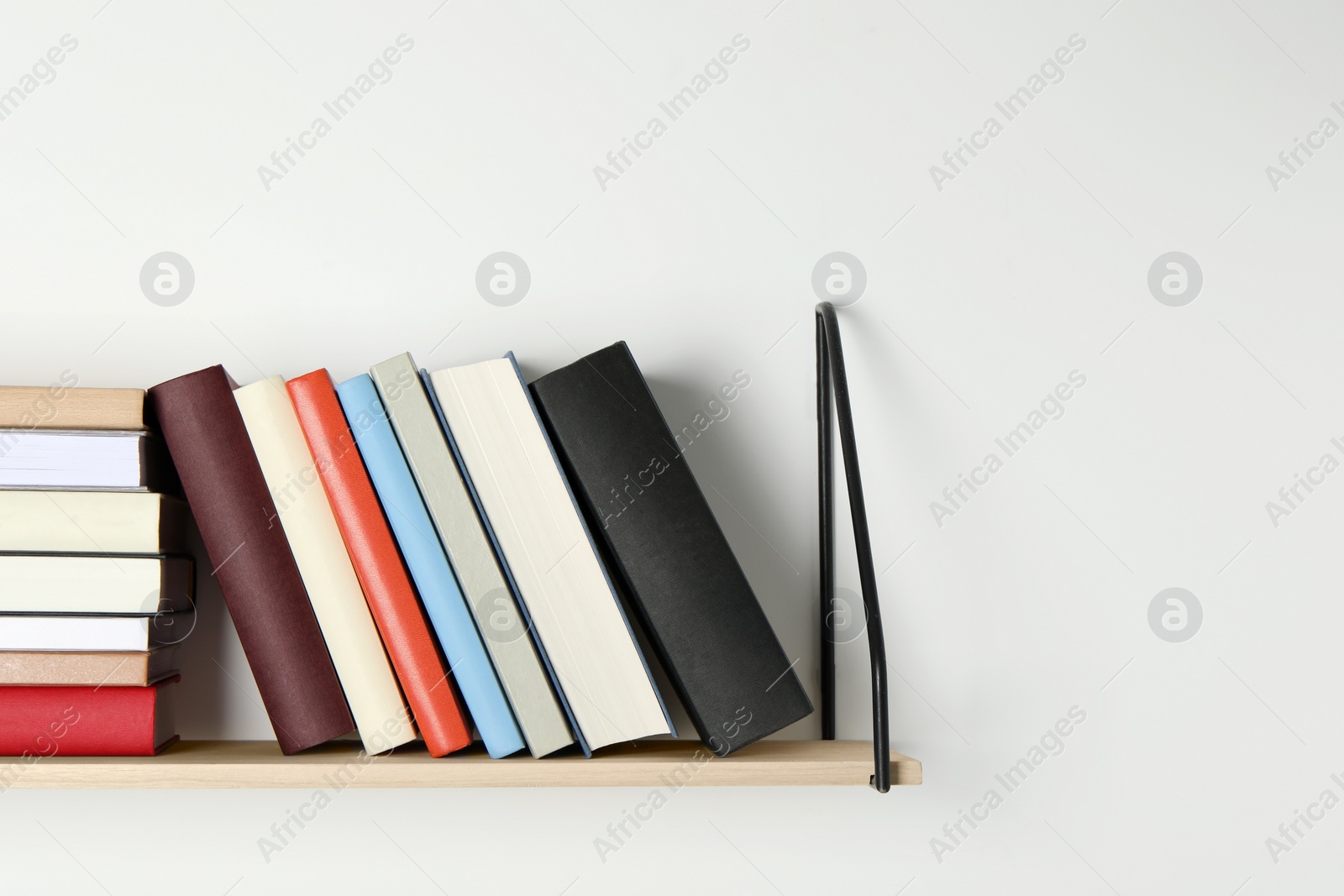 Photo of Wooden shelf with many hardcover books on white wall. Space for text