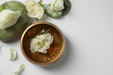 Photo of Tibetan singing bowl with water, beautiful rose flowers and spa stones on white background, flat lay. Space for text