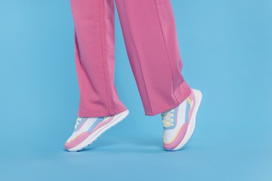 Woman wearing pair of new stylish sneakers on light blue background, closeup