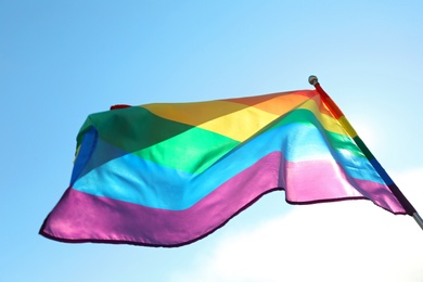 Photo of Bright rainbow gay flag fluttering against blue sky, bottom view. LGBT community