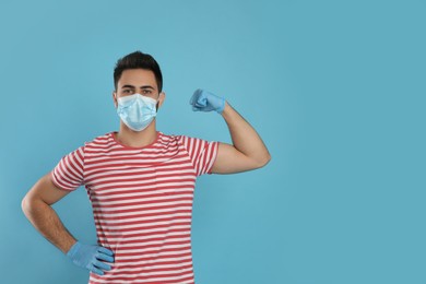 Photo of Man with protective mask and gloves showing muscles on light blue background, space for text. Strong immunity concept