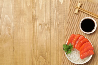 Delicious salmon sashimi served with funchosa, soy sauce and parsley on wooden table, top view. Space for text