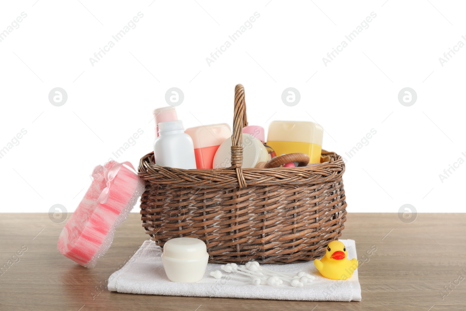 Photo of Wicker basket full of different baby cosmetic products, bathing accessories and toys on wooden table against white background