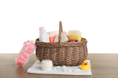 Photo of Wicker basket full of different baby cosmetic products, bathing accessories and toys on wooden table against white background