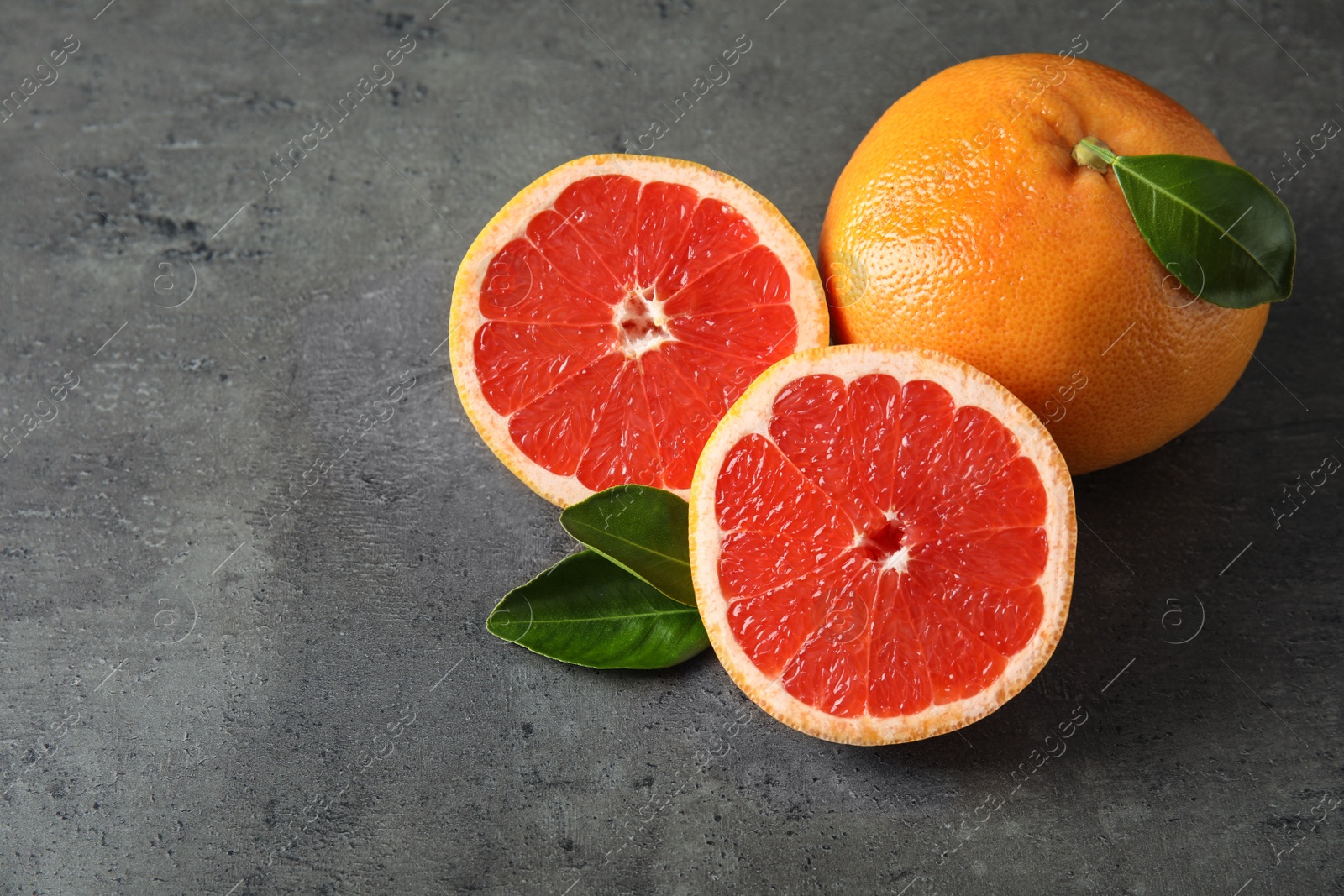 Photo of Fresh tasty grapefruits with leaves on grey table. Space for text