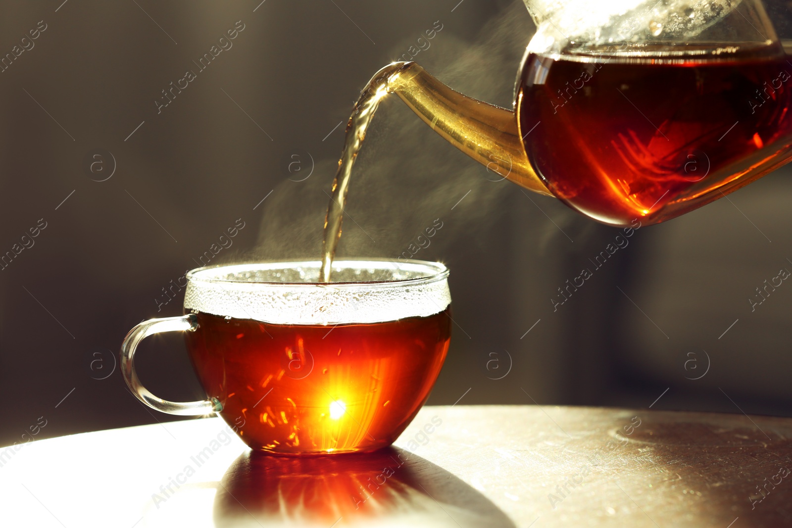 Photo of Pouring fresh hot tea from teapot into cup against blurred background, closeup