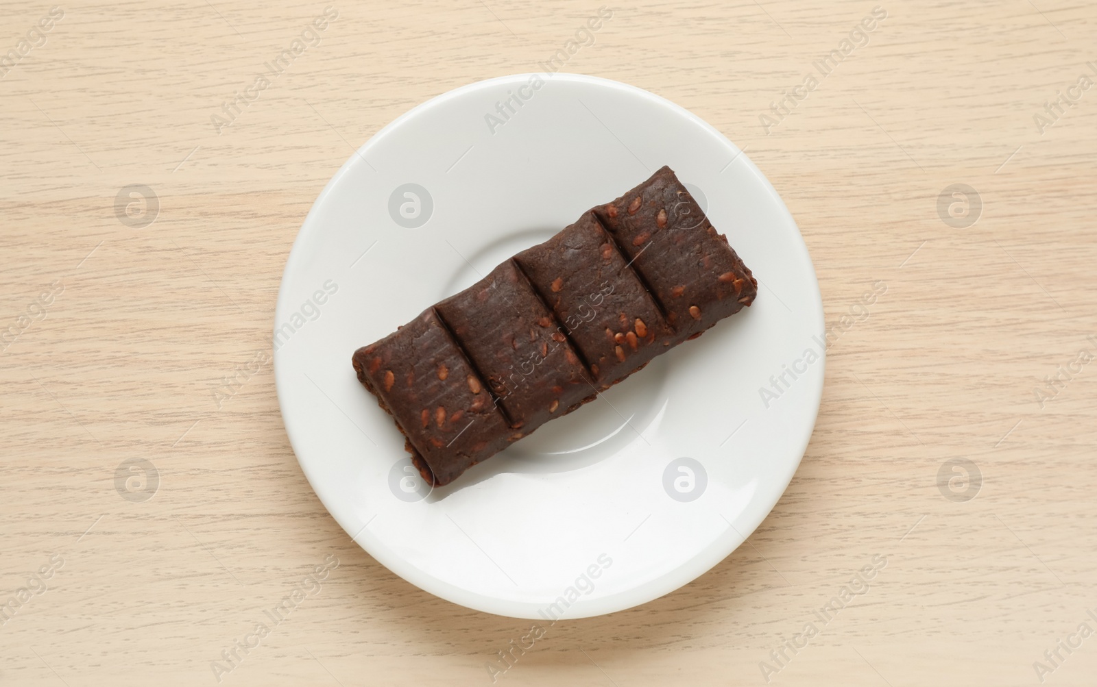 Photo of White plate with delicious and healthy hematogen bar  on wooden table, top view