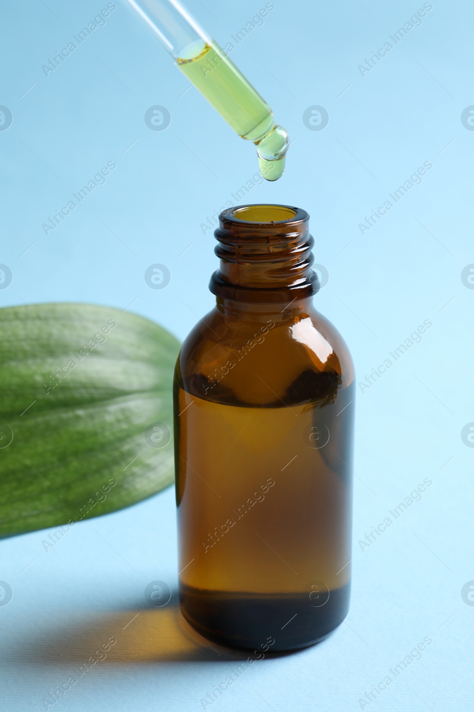 Photo of Dripping cosmetic oil from pipette into bottle on light blue background