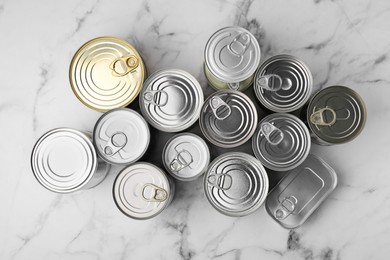 Many closed tin cans on white marble table, flat lay