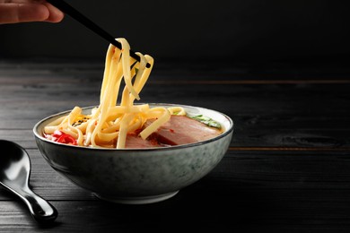 Woman eating delicious ramen with chopsticks at black wooden table, closeup and space for text. Noodle soup