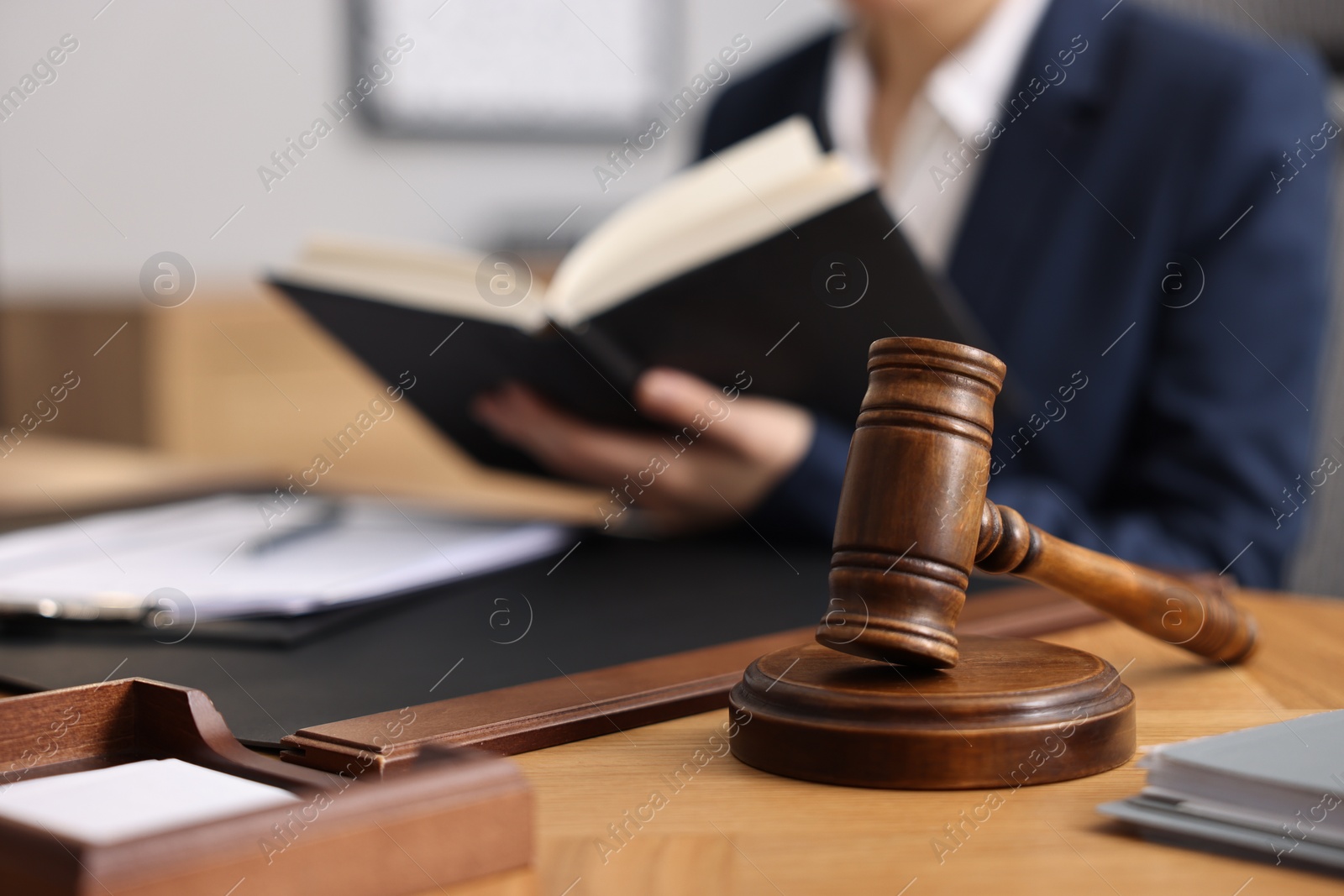 Photo of Notary reading book at wooden table in office, focus on gavel