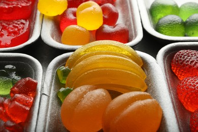 Photo of Different delicious gummy candies in containers, closeup