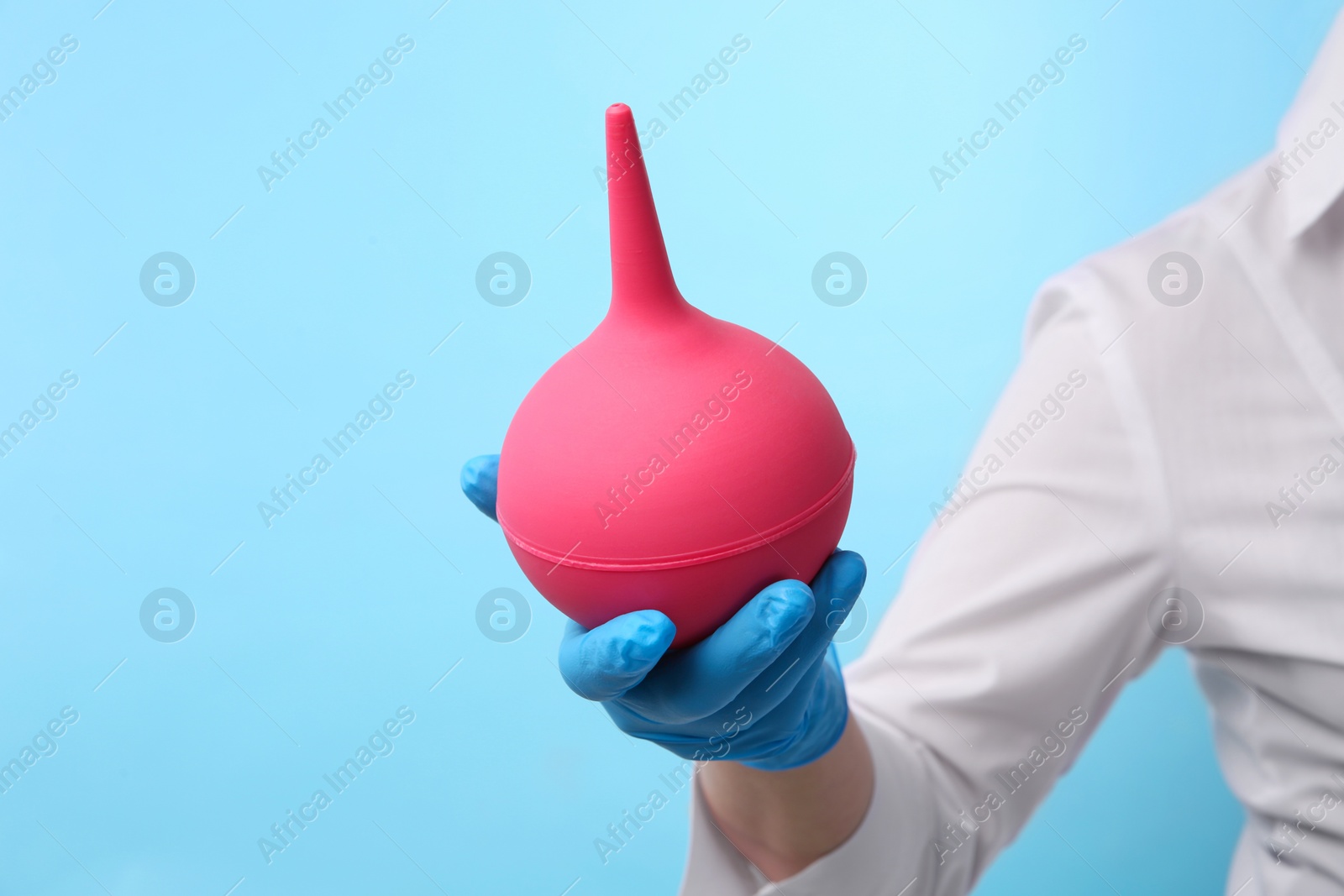 Photo of Doctor holding pink enema on light blue background, closeup