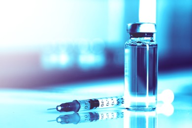Image of Syringe and glass vial with medication on mirror surface, toned in light blue