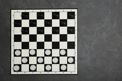 Checkerboard with game pieces on grey table, top view. Space for text