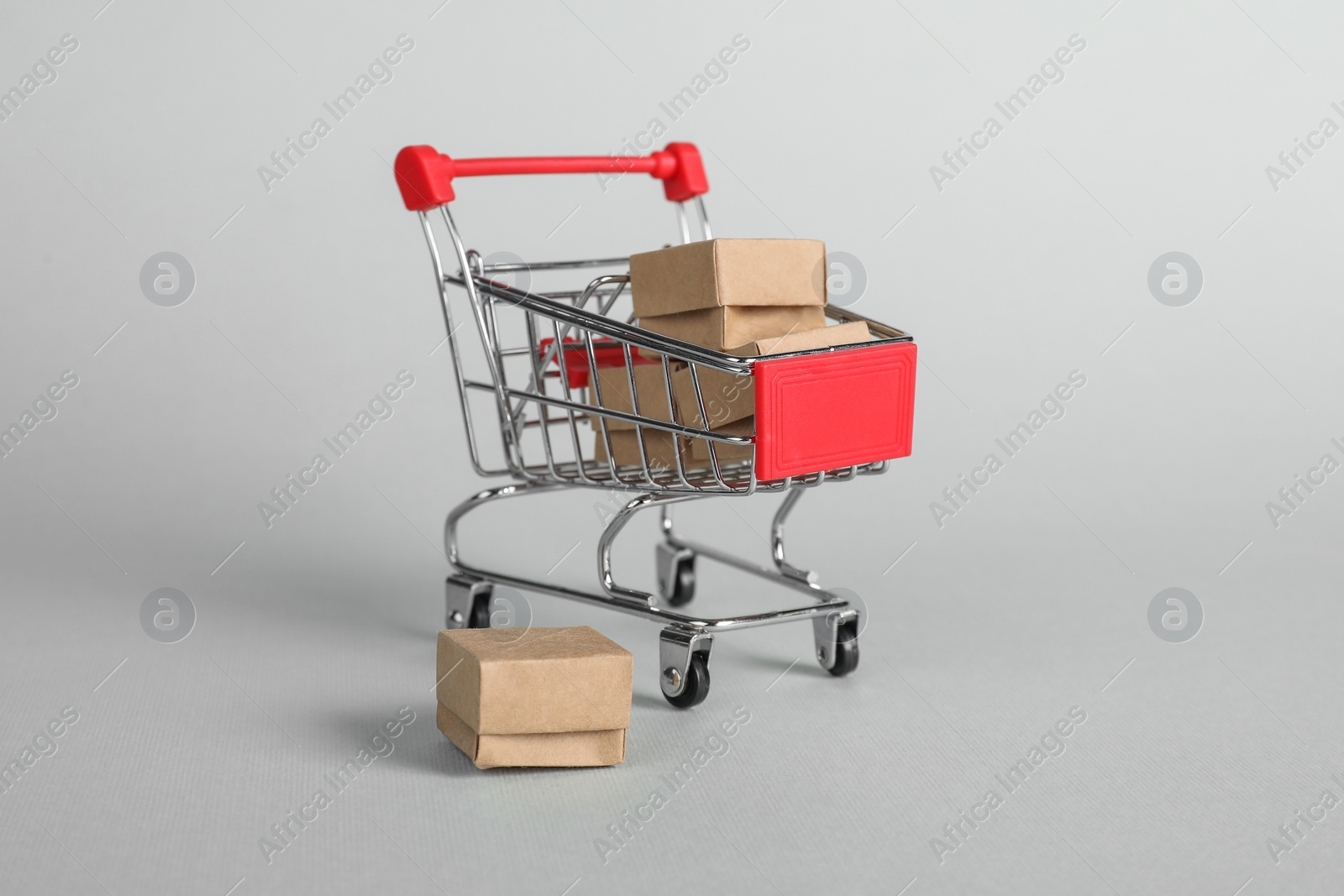 Photo of Small metal shopping cart with cardboard boxes on light background