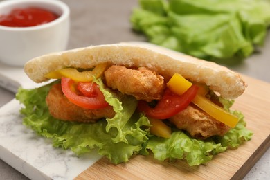 Photo of Delicious pita sandwich with fried fish, pepper, tomatoes and lettuce on table, closeup