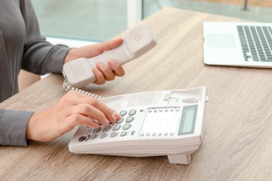 Photo of Woman dialing number on telephone at table indoors, closeup