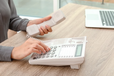 Woman dialing number on telephone at table indoors, closeup