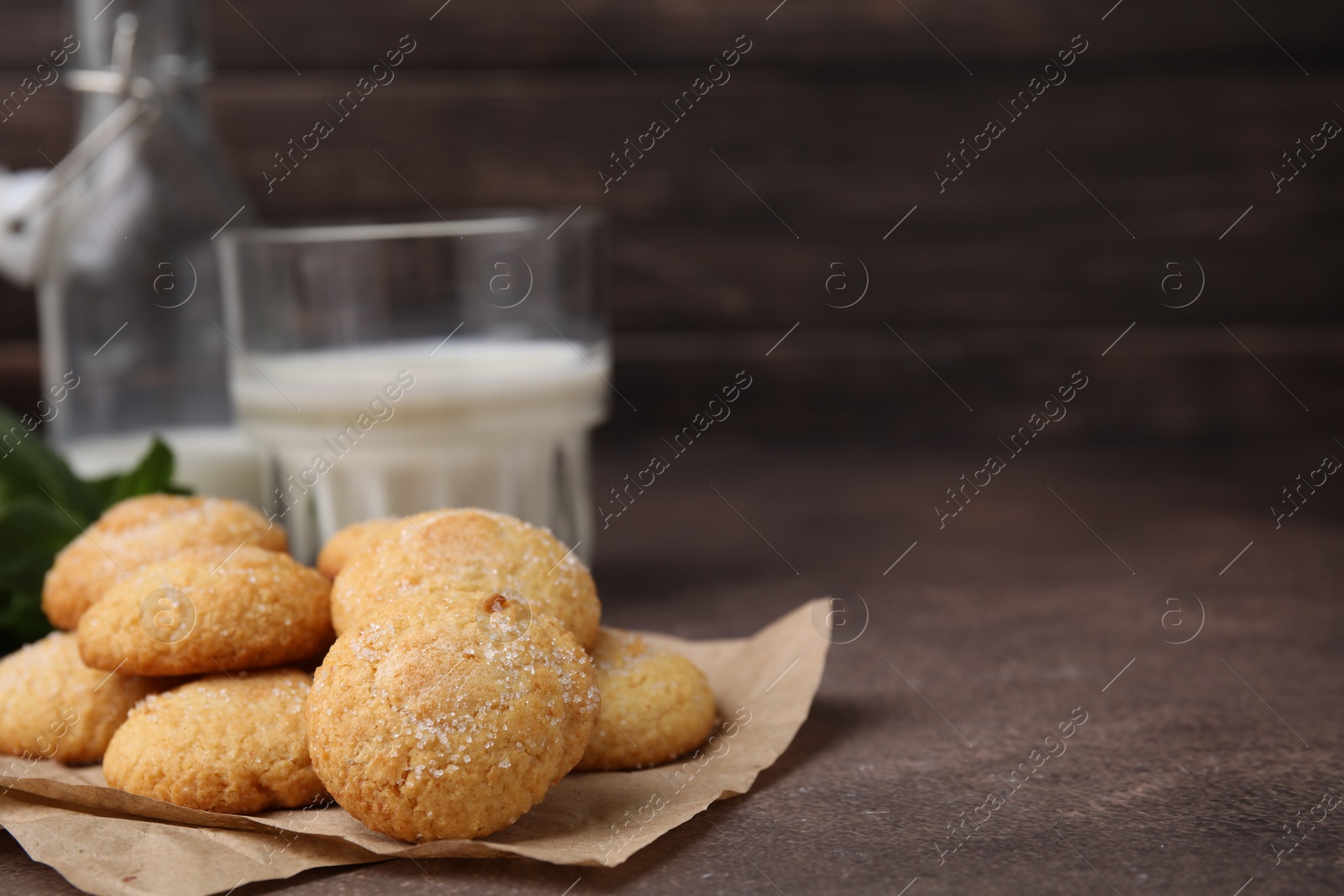 Photo of Tasty sweet sugar cookies and milk on brown table, closeup. Space for text