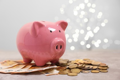 Photo of Piggy bank with euro banknotes and coins on grey table against blurred lights, space for text