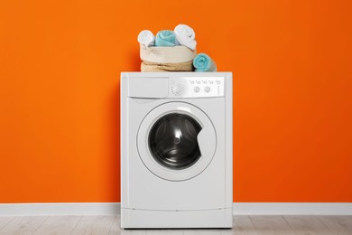 Photo of Washing machine with clean towels near orange wall indoors. Interior design
