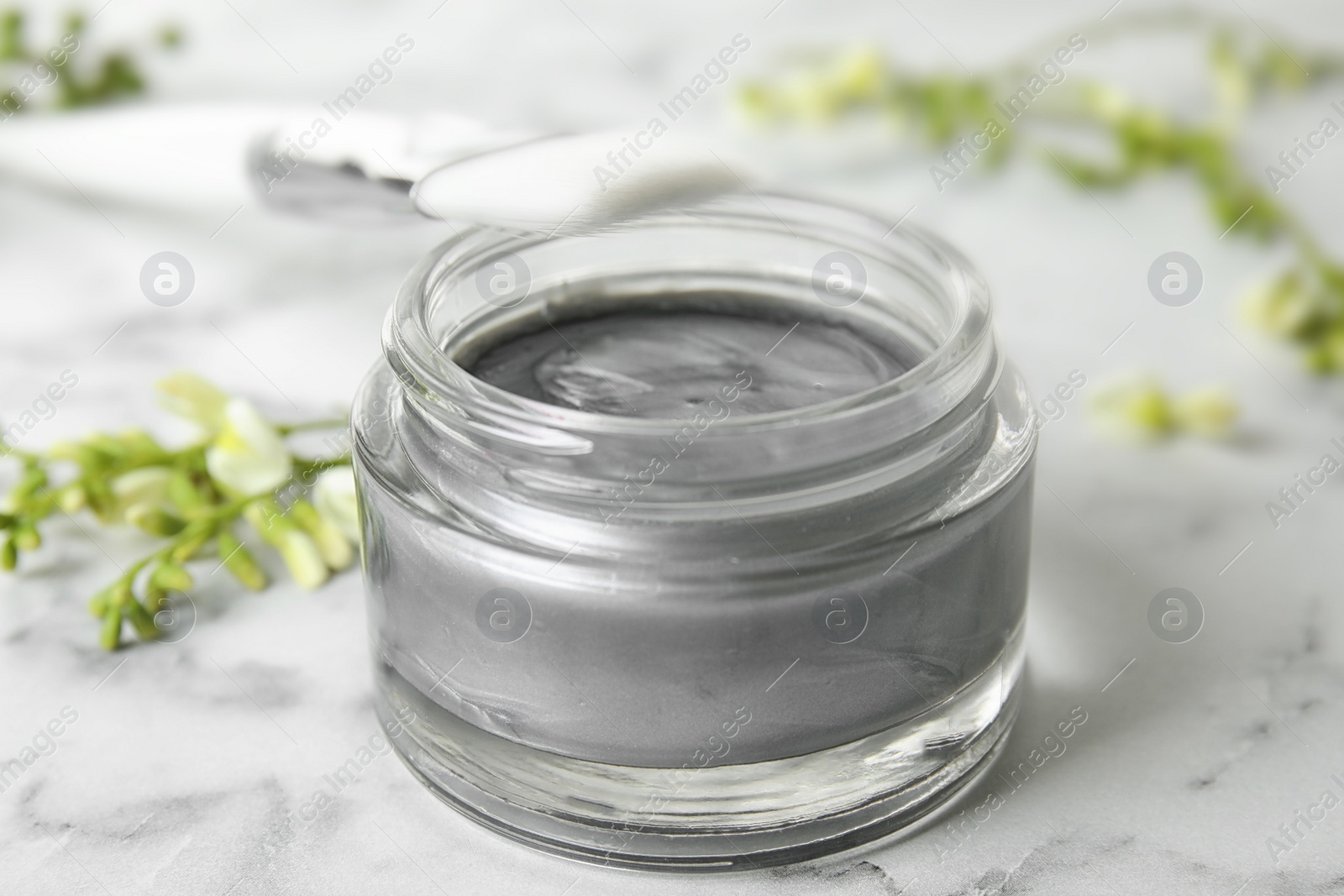 Photo of Professional face mask with brush and flowers on white marble table, closeup