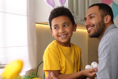 Photo of Happy African American father and his cute son with Easter eggs in kitchen