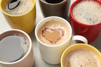Many cups with different aromatic coffee on light grey table, closeup