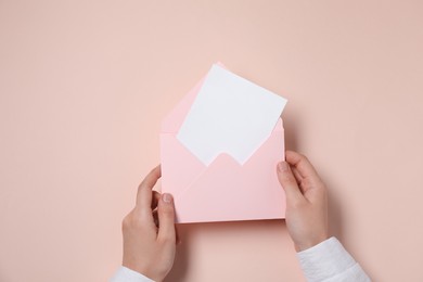 Woman holding letter envelope with card at beige table, top view