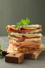 Stack of tasty sandwiches with ham, parsley and melted cheese on grey table, closeup
