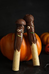 Photo of Delicious sticks with chocolate decorated as monsters on dark background. Halloween treat