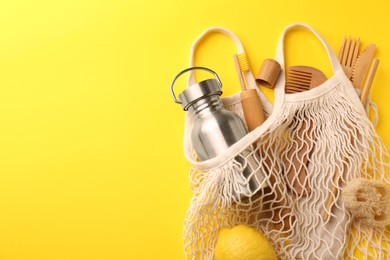 Photo of Fishnet bag with different items on yellow background, top view and space for text. Conscious consumption