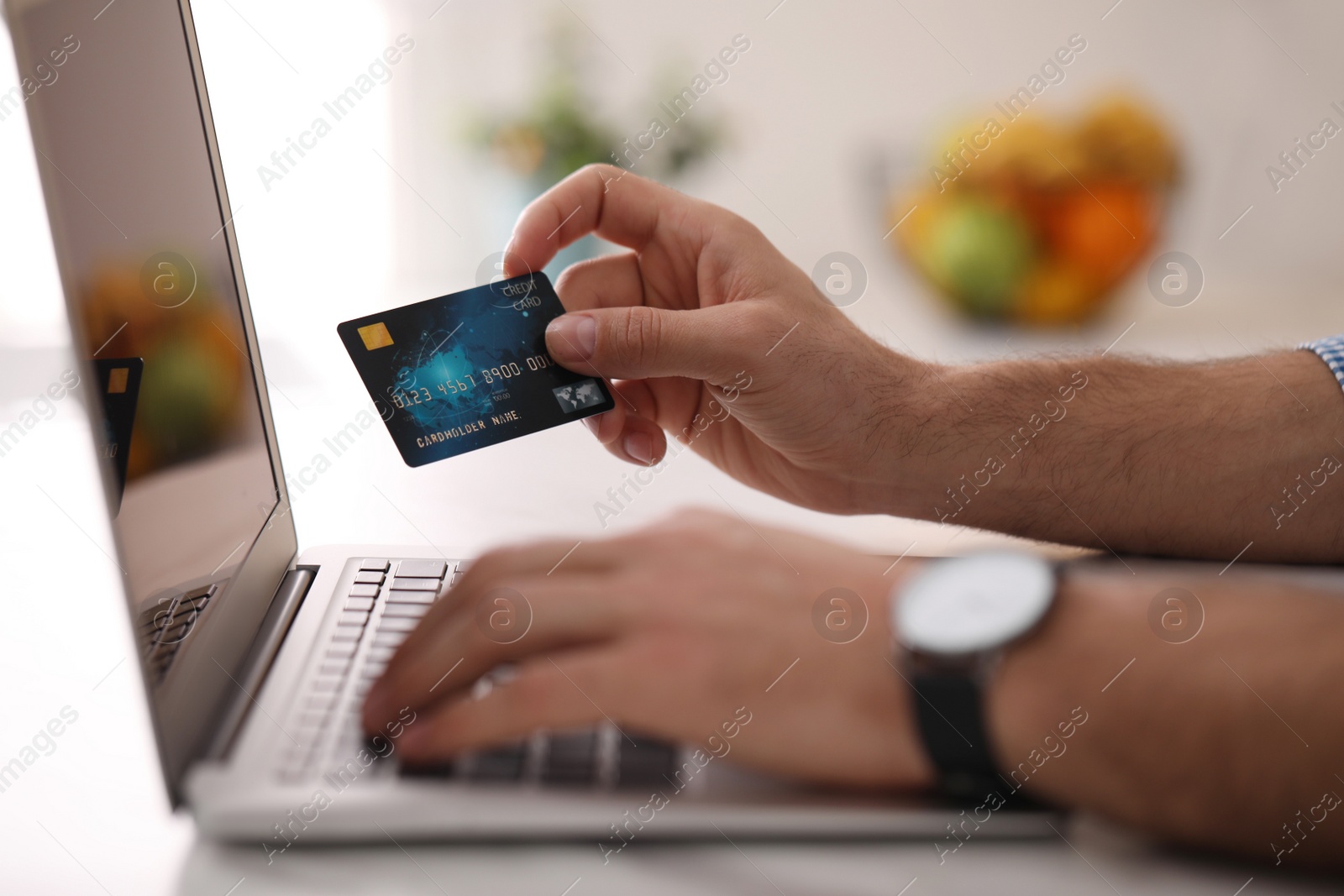 Photo of Man using laptop and credit card for online payment at table in kitchen, closeup