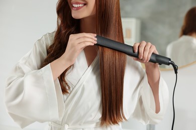 Photo of Young woman using hair iron indoors, closeup