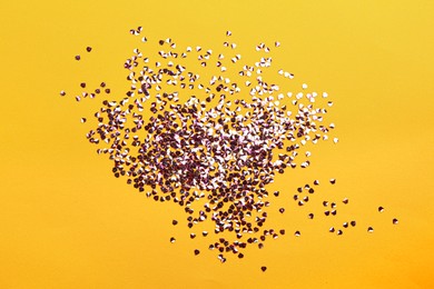 Photo of Shiny bright violet glitter on yellow background, flat lay