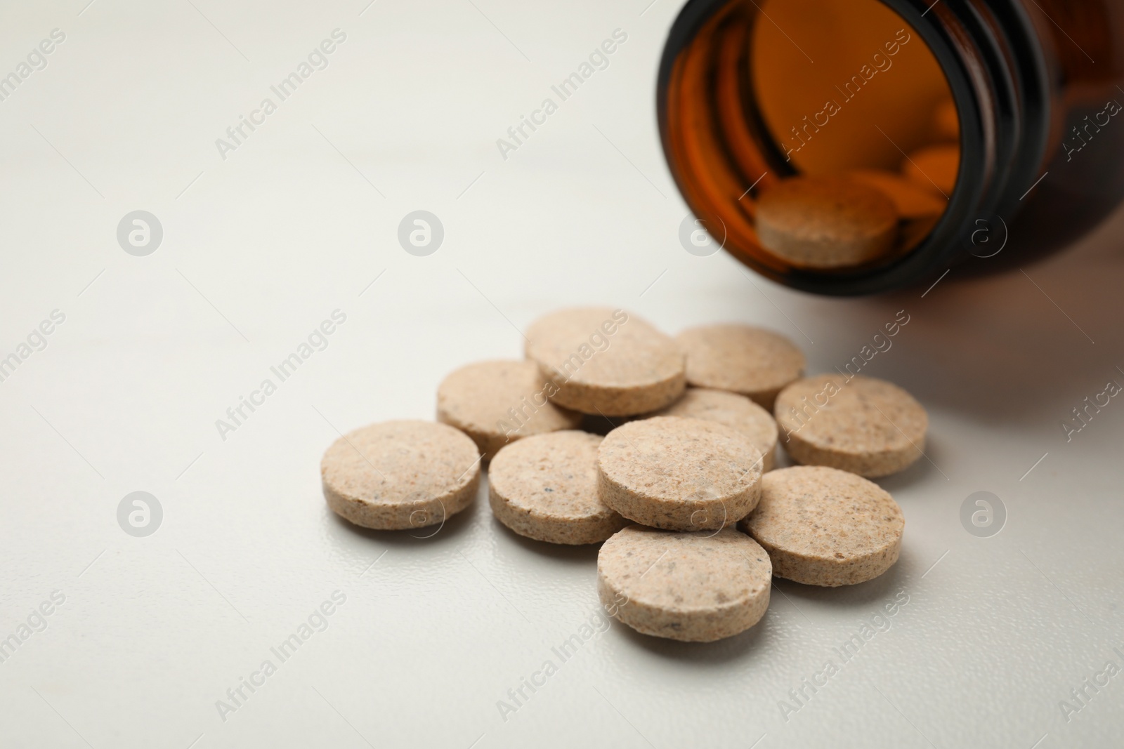 Photo of Overturned bottle with dietary supplement pills on white table, closeup