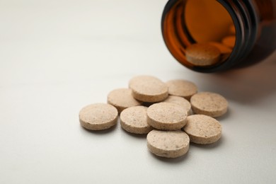 Photo of Overturned bottle with dietary supplement pills on white table, closeup