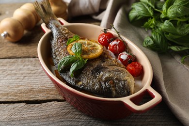 Delicious roasted dorado fish with tomatoes, basil and lemon on wooden table, closeup