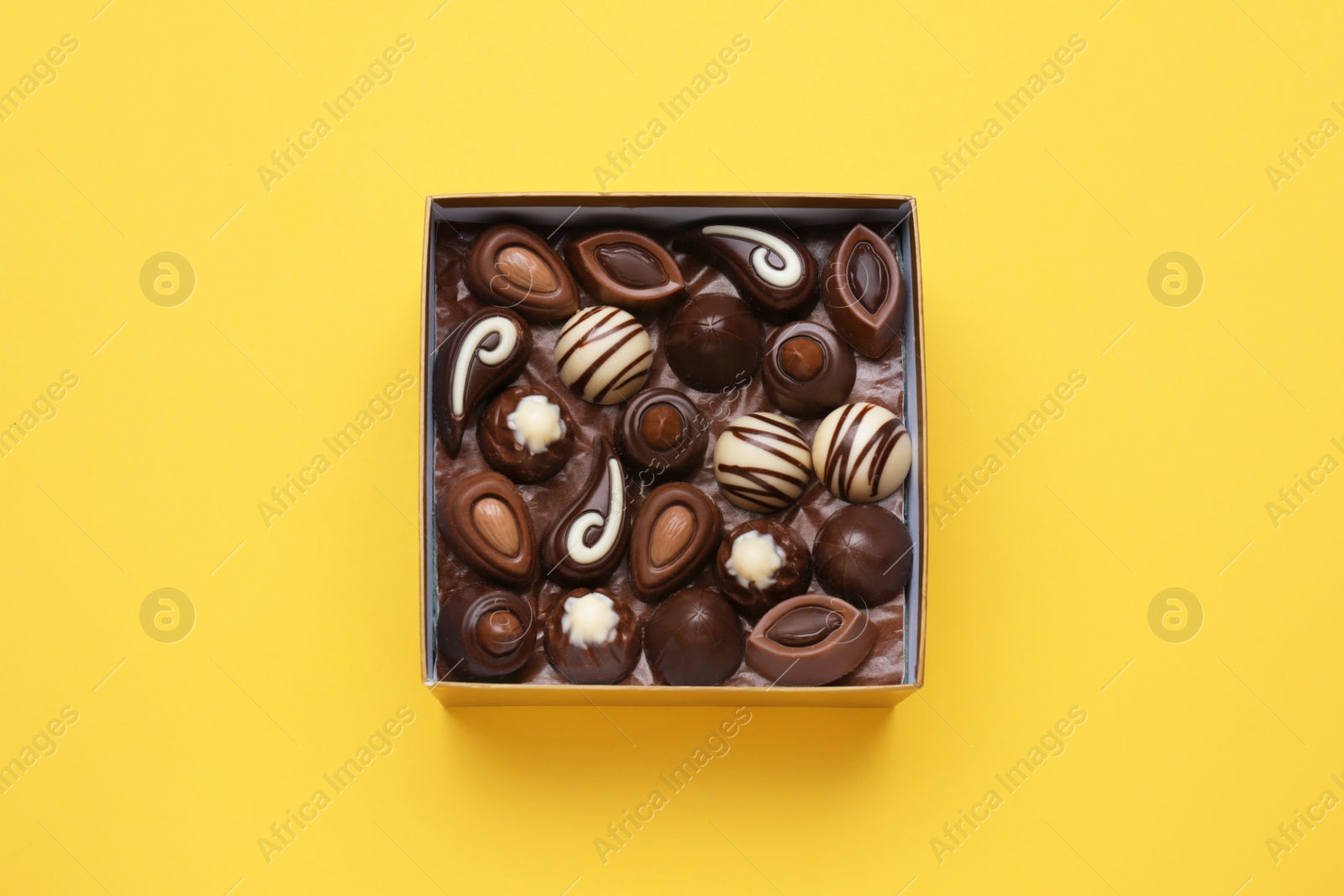 Photo of Box of delicious chocolate candies on yellow background, top view