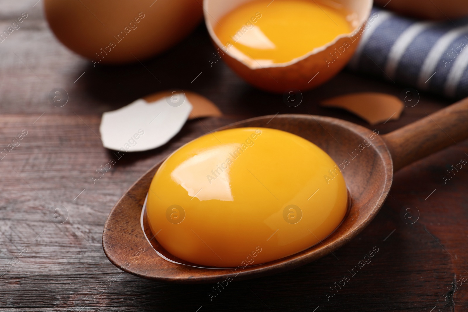 Photo of Spoon with raw egg yolk on wooden table, closeup