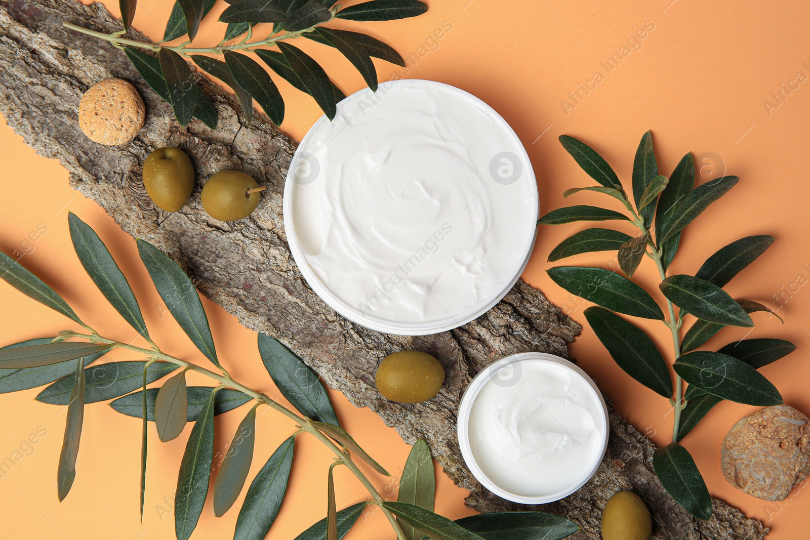 Photo of Flat lay composition with jars of cream and olives on pale orange background