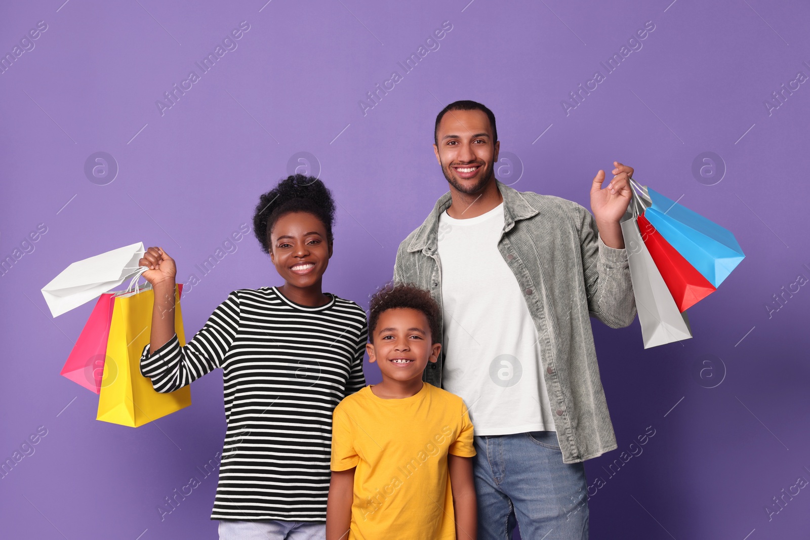 Photo of Family shopping. Happy parents and son with colorful bags on violet background