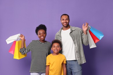 Photo of Family shopping. Happy parents and son with colorful bags on violet background