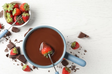 Photo of Dipping strawberry into fondue pot with chocolate on white table, top view. Space for text