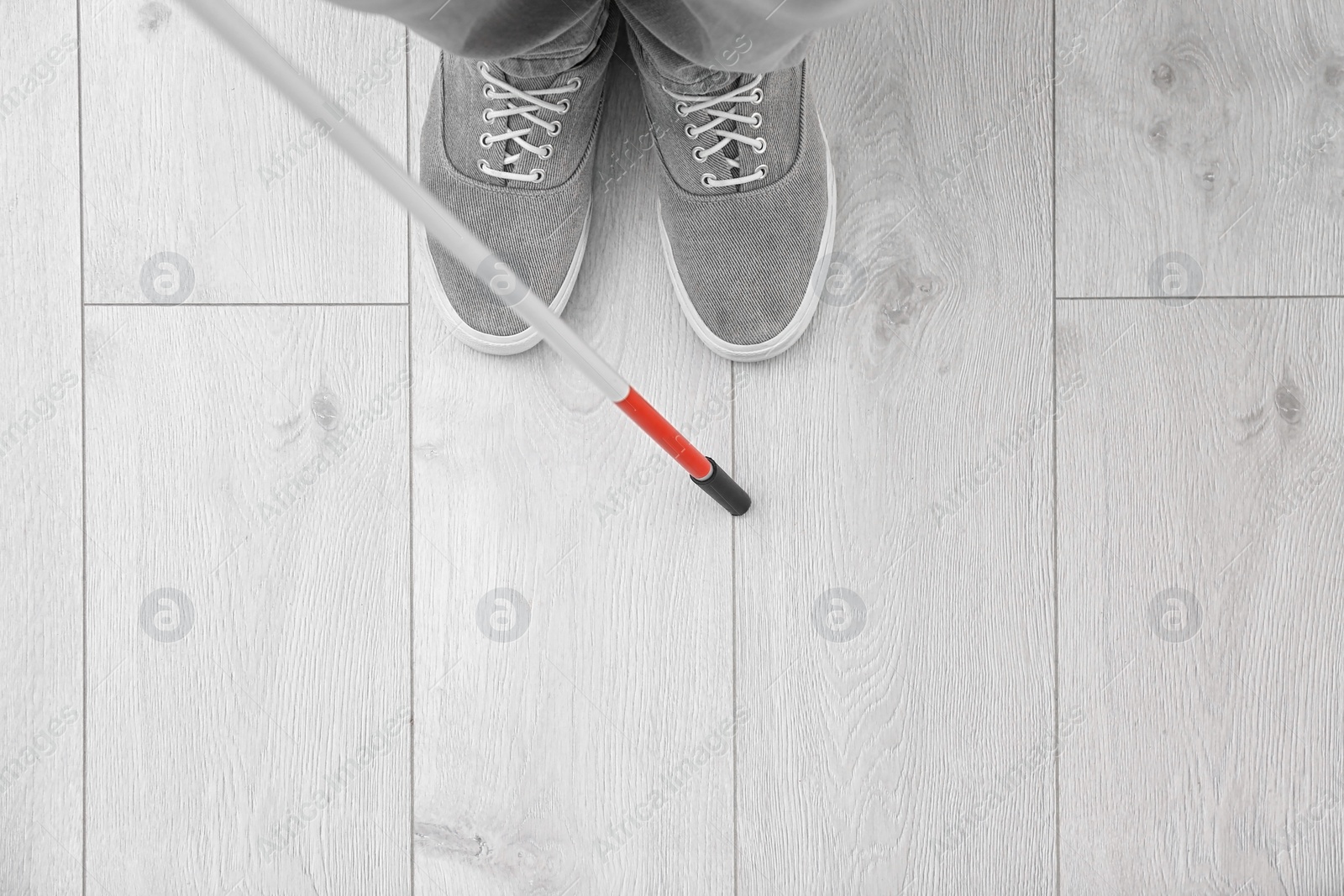 Photo of Blind person with long cane standing indoors, top view. Space for text