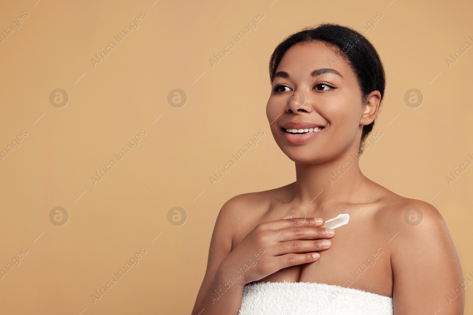 Photo of Young woman applying cream onto body on beige background. Space for text