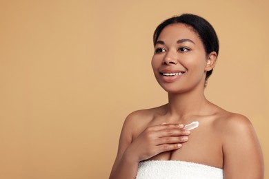 Young woman applying cream onto body on beige background. Space for text