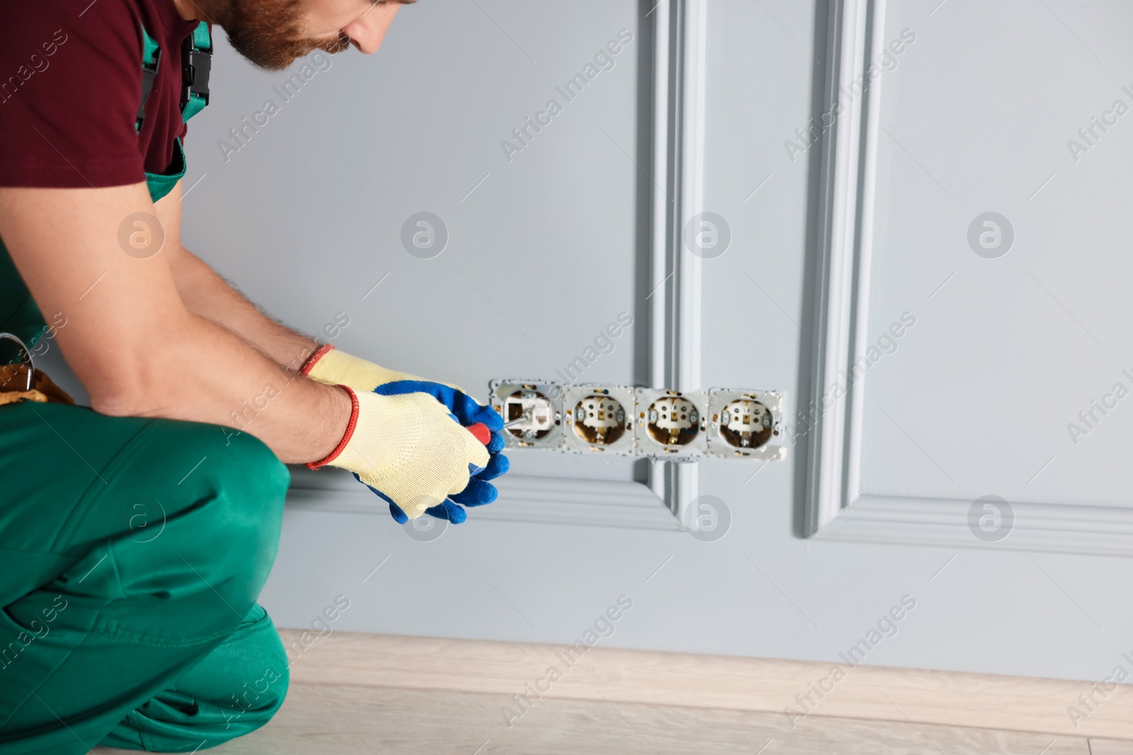 Photo of Electrician with screwdriver repairing power sockets indoors, closeup